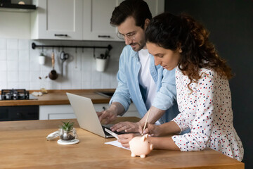 Concentrated millennial spouses calculating family budget paying utility bills online using laptop....