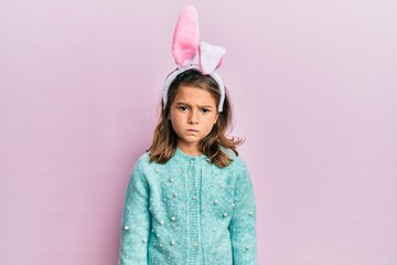 Little beautiful girl wearing cute easter bunny ears skeptic and nervous, frowning upset because of...