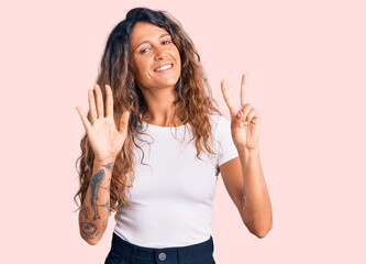 Young hispanic woman with tattoo wearing casual white tshirt showing and pointing up with fingers number seven while smiling confident and happy.