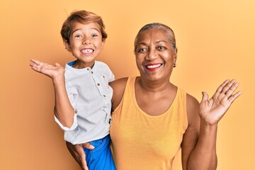 Hispanic grandson and grandmother together over yellow background celebrating achievement with...