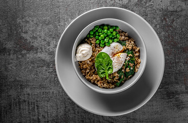 oatmeal with poached egg and green pea in a bowl on Dark grey black slate background