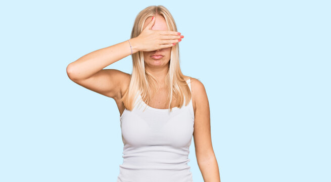 Young blonde girl wearing casual style with sleeveless shirt covering eyes with hand, looking serious and sad. sightless, hiding and rejection concept