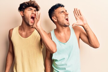 Young gay couple wearing casual clothes shouting and screaming loud to side with hand on mouth....