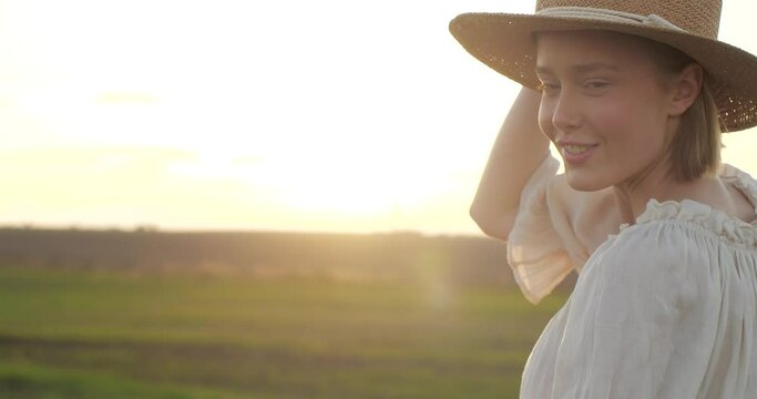 Charming and beautiful country Woman enjoying nature and having fun at Field. Happy with a feeling of Absolute Freedom, turning to the Camera with Cute Smile. Wearing Straw Hat. Looking pleasant.