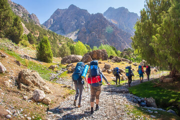 Hikers with backpacks walking in mountains. Group of friends in Fann mountains, Tajikistan. Mountain trail. Tourists hiking.