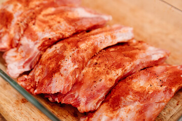 raw pork ribs sprinkle with salt, black pepper and paprika in a glass baking tray on a wooden cutting board. cooking meat at home. Cook.