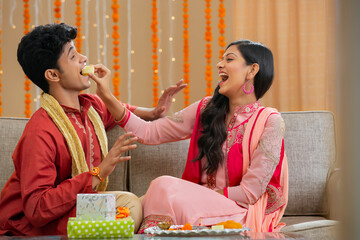 sister stuffing barfi in brother's mouth	