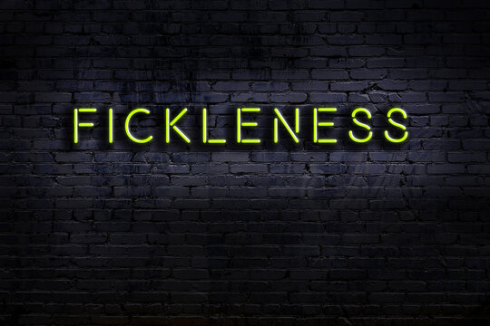 Neon sign. Word fickleness against brick wall. Night view