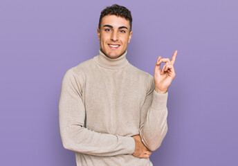 Hispanic young man wearing casual turtleneck sweater smiling happy pointing with hand and finger to the side