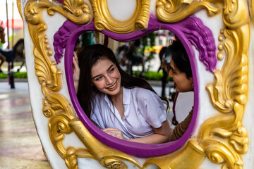 The asian couple lover happily sitting in the carousel of the amusement park.
