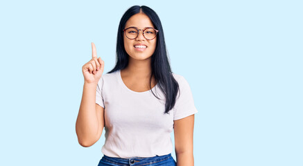 Young beautiful asian girl wearing casual clothes and glasses pointing finger up with successful idea. exited and happy. number one.