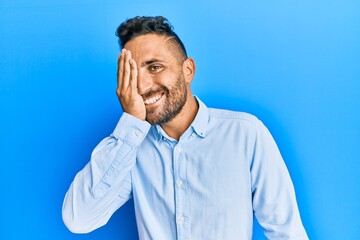 Obraz premium Handsome man with beard wearing casual clothes covering one eye with hand, confident smile on face and surprise emotion.