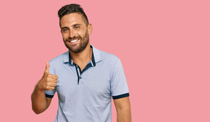 Handsome man with beard wearing casual clothes doing happy thumbs up gesture with hand. approving expression looking at the camera showing success.