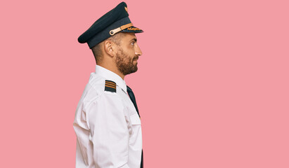 Handsome man with beard wearing airplane pilot uniform looking to side, relax profile pose with...