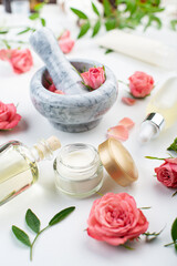 Handmade rose cosmetics concept of mortar and pestle with rose buds with dropper and bottles with serum and oil on white background