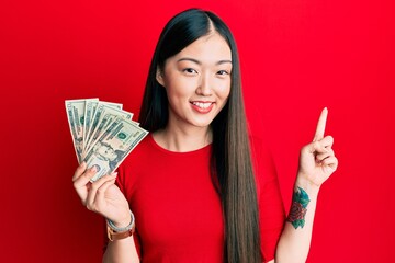 Young chinese woman holding 20 dollars banknote smiling happy pointing with hand and finger to the side