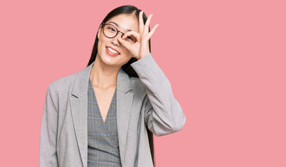 Young chinese woman wearing business clothes smiling happy doing ok sign with hand on eye looking through fingers