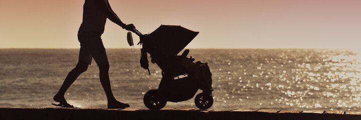Silhouette mother pulling baby stroller against beach sunset