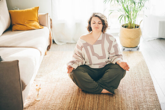  Plus size woman doing yoga and meditation at home.