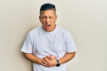 Young latin man wearing casual white t shirt with hand on stomach because nausea, painful disease feeling unwell. ache concept.