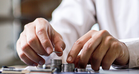 A close-up view of a businessman using two hands to stack coins in a row, he always invested his money to grow more. The idea of bringing money to pass the money.