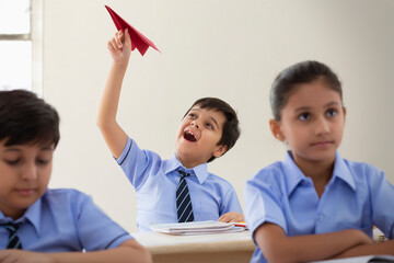 school boy playing with paper plane in class	