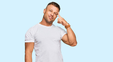 Fototapeta premium Handsome muscle man wearing casual white tshirt smiling pointing to head with one finger, great idea or thought, good memory