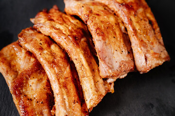 fried with spices pork ribs in a glass baking sheet on a stone black background. cooked meat at home. Barbecue.