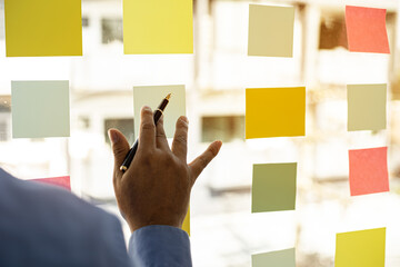 Business men are writing on a post-it that is placed in the glass of the conference room to...