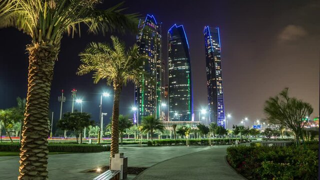Famous towers buildings in Abu Dhabi night timelapse hyperlapse from park with palms. United Arab Emirates. Five towers complex is the third tallest building in Abu Dhabi.