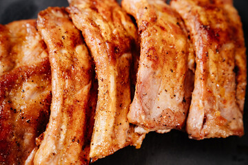 fried with spices pork ribs in a glass baking sheet on a stone black background. cooked meat at home. Barbecue.