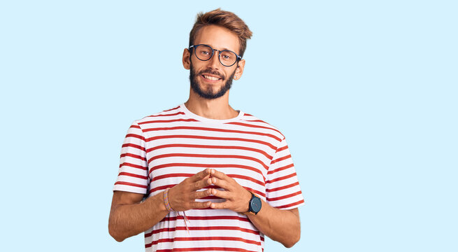 Handsome blond man with beard wearing casual clothes and glasses hands together and fingers crossed smiling relaxed and cheerful. success and optimistic