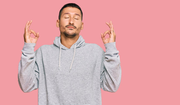 Handsome man with tattoos wearing casual sweatshirt relax and smiling with eyes closed doing meditation gesture with fingers. yoga concept.