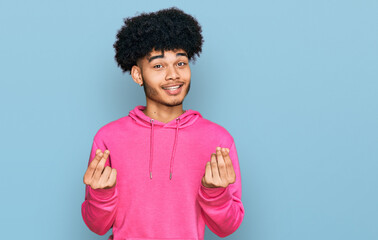 Young african american man with afro hair wearing casual pink sweatshirt doing money gesture with hands, asking for salary payment, millionaire business