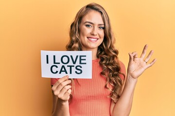 Fototapeta na wymiar Young blonde girl holding paper with i love cats phrase doing ok sign with fingers, smiling friendly gesturing excellent symbol