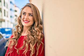 Fototapeta premium Young blonde girl smiling happy leaning on the wall at the city.