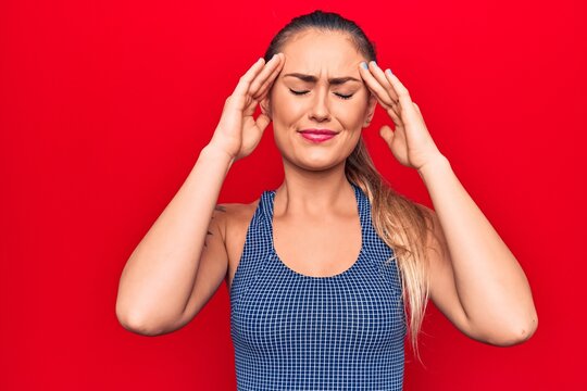 Young beautiful blonde woman wearing sporty t-shirt standing over isolated red background with hand on head, headache because stress. Suffering migraine.