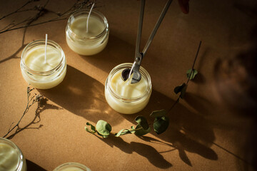 Handmade candle from paraffin and soy wax in glass with flowers and tools on craft background. Let flay. Candle making