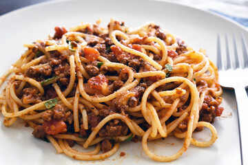 Spaghetti Bolognese with minced beef, onion, chopped tomato, garlic, olive oil, stock cube, tomato puree and Italian herb. Traditional Italian food in white plate with a fork.