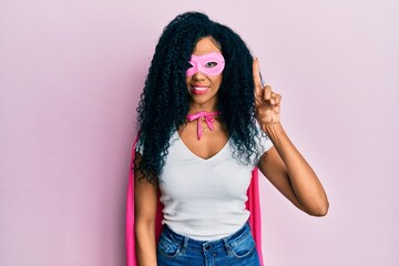 Middle age african american woman wearing super hero costume showing and pointing up with finger number one while smiling confident and happy.