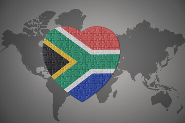 puzzle heart with the national flag of south africa on a world map background. © luzitanija