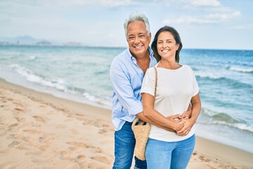 Middle age hispanic couple smiling happy and hugging walking at the beach