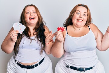 Plus size caucasian sisters woman holding poker chips and cards celebrating victory with happy smile and winner expression with raised hands