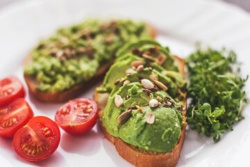 Vegan avocado sandwich with tomatoes and microgreens on a white plate