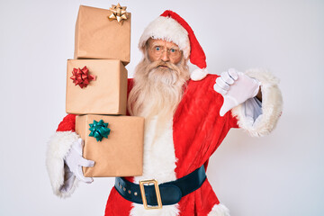 Old senior man with grey hair and long beard wearing santa claus costume holding presents with angry face, negative sign showing dislike with thumbs down, rejection concept