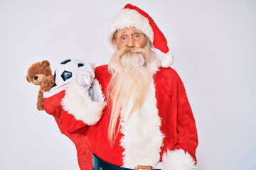 Old senior man with grey hair and long beard wearing santa claus costume holding mustache relaxed with serious expression on face. simple and natural looking at the camera.
