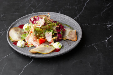 A tasty and sweet salad with pear, tomato, mozzarella cheese and fresh lettuce, dressed with a red and green sauces. Close-up on a grey round plate on a black marble background. Healthy food.