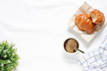 Top view of hot coffee cup beside fresh croissant on white tablecloths.