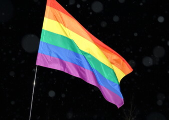 rainbow flag symbolizing LGBT groups waves against black sky close up