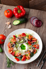 Greek salad with fresh vegetables: tomato, cucumber, red bel pepper, lettuce, onion, olives and cheese. Close-up on a white round plate on a wooden background. Salad menu with ingredients.